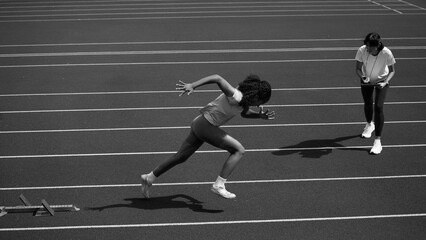 Female sprinter launching from starting blocks beside her coach